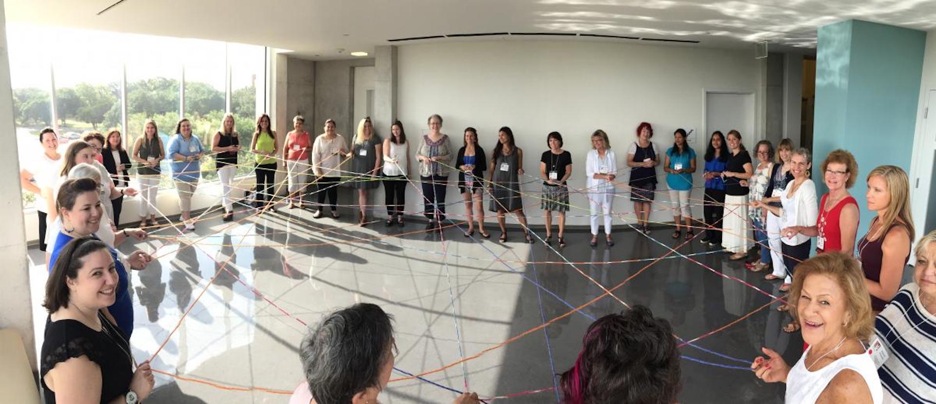 A circle of Family Engagement Coordinators all holding a piece of yarn creating a web.