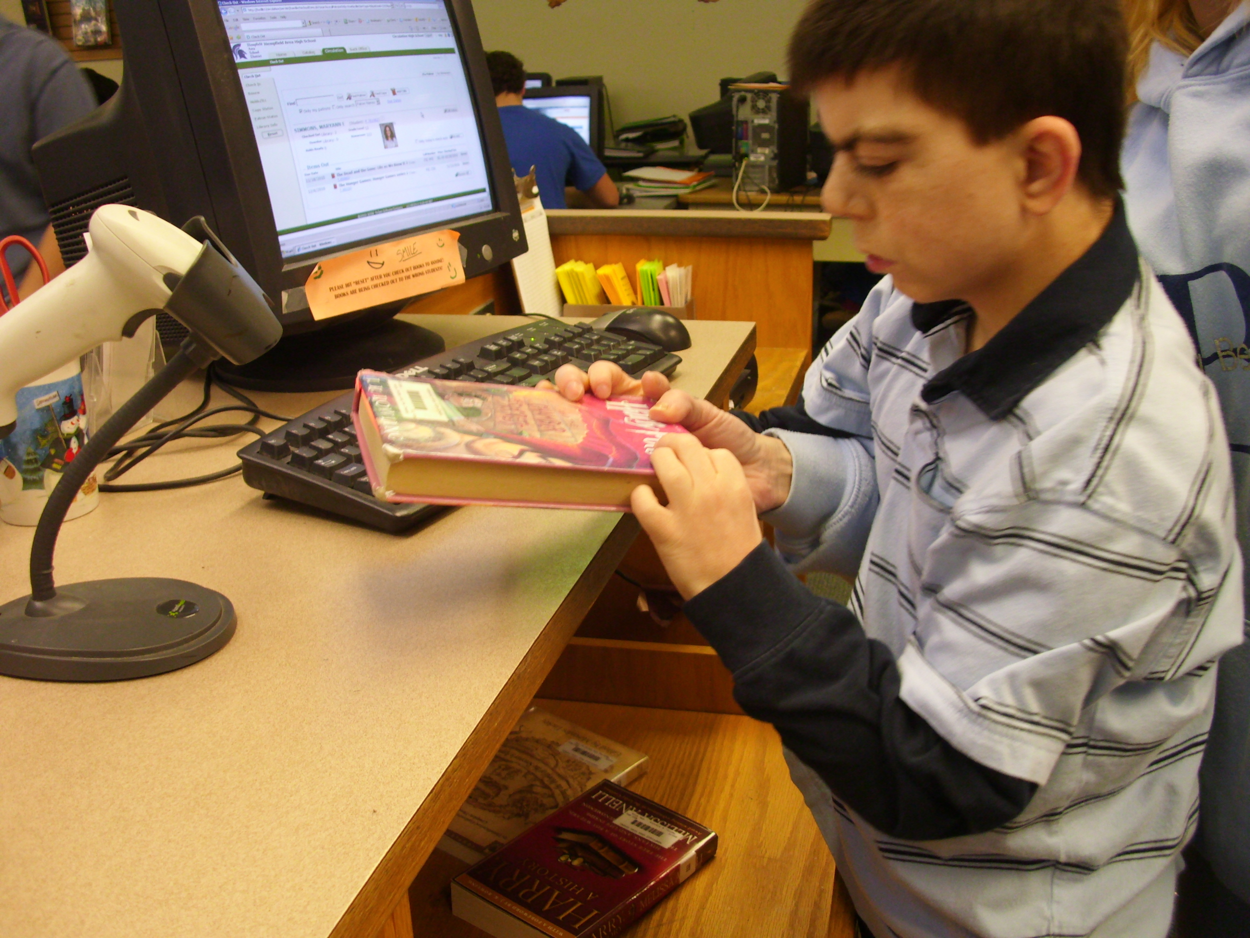 A young man is standing at a counter checking in a book.