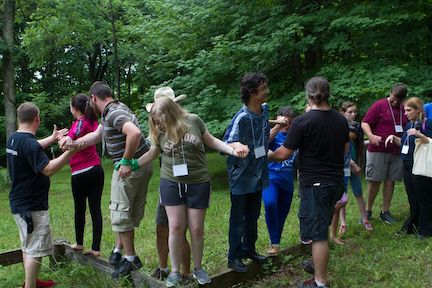 Several young adults holding hands on balance beam.