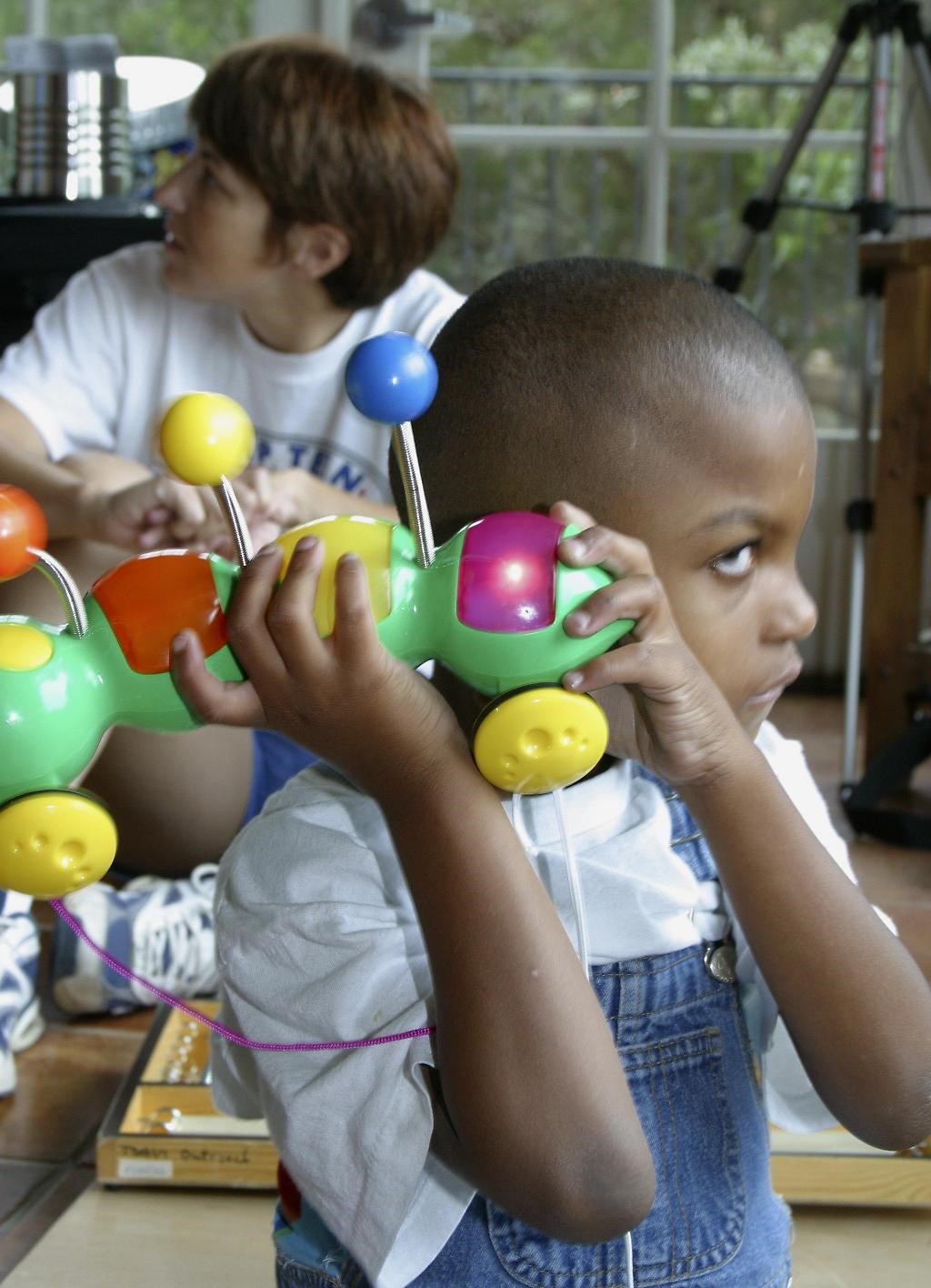 A young boy holding a toy near his ear.