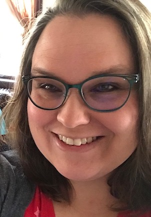 Headshot of a smiling adult woman with chin-length brown hair and green glasses.